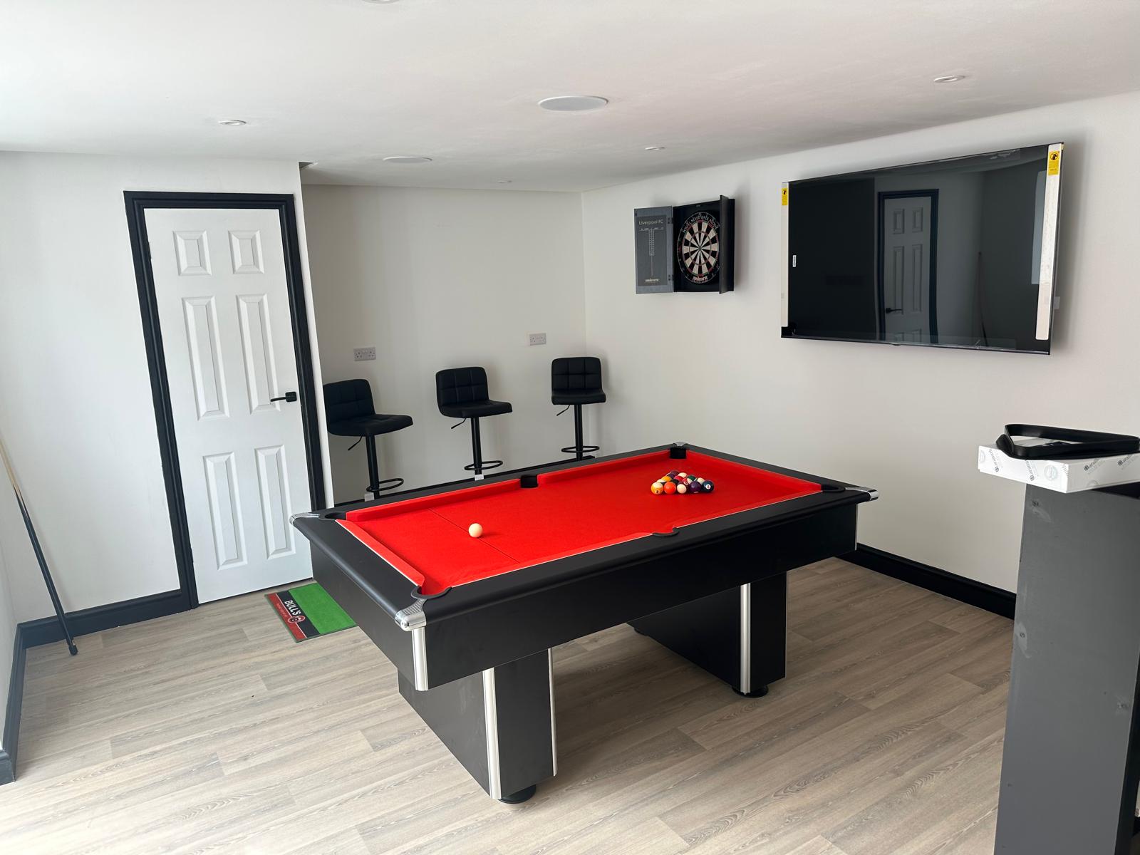 A finished games room with a pool table, dartboard cabinet and wall-mounted TV